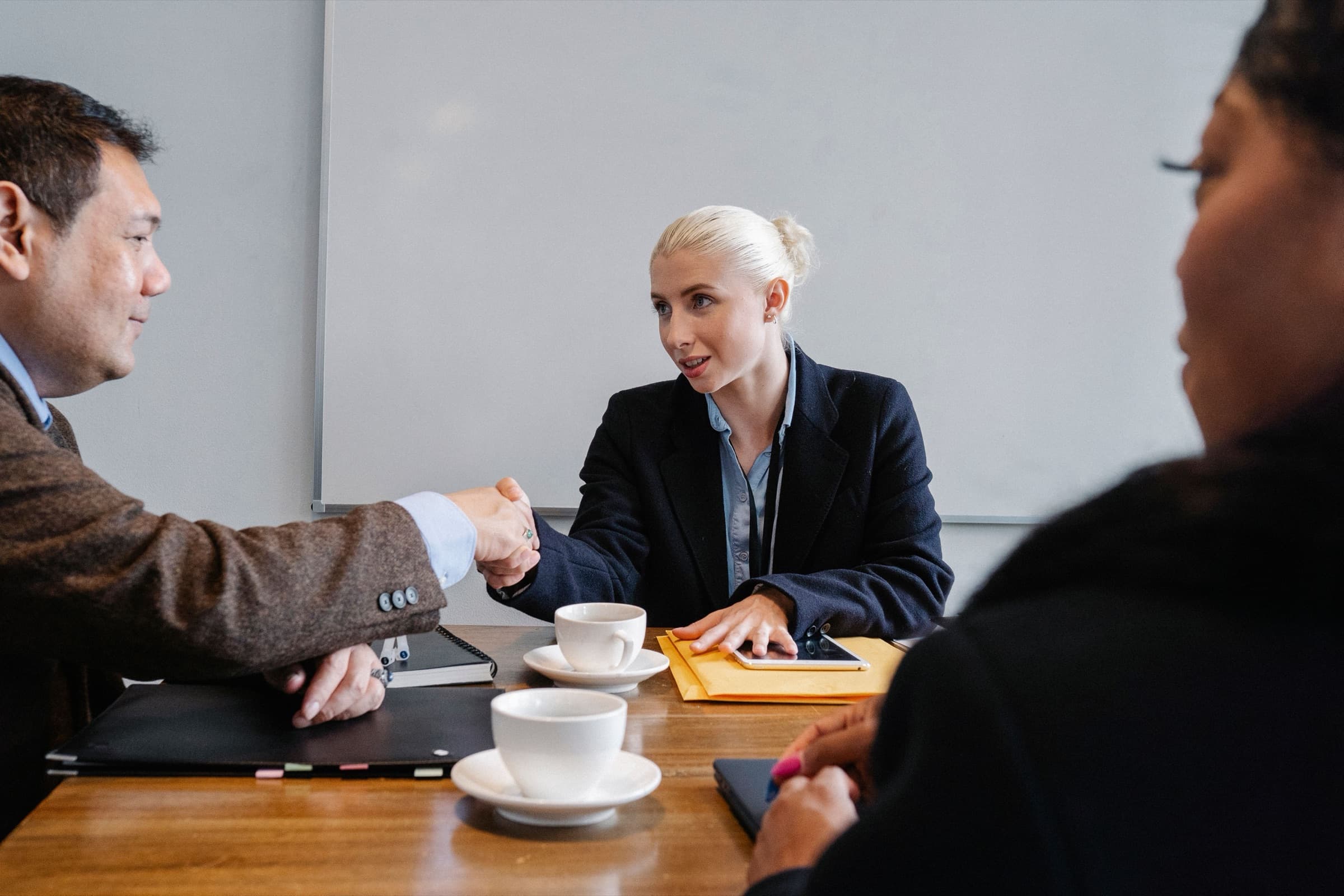 Two people shaking hands across a meeting table as a third looks on